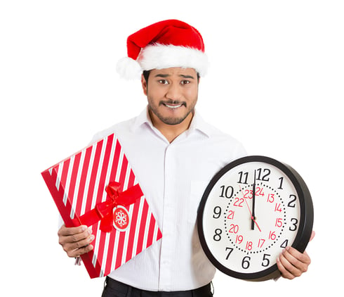 Closeup portrait of worried young man wearing red santa claus hat, holding clock and gift in hands, isolated on white background. Negative emotion facial expression. Last minute christmas shopping-1